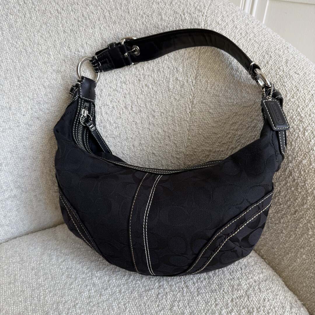 A black Coach croissant shoulder bag with silver hardware, displayed on a neutral background.