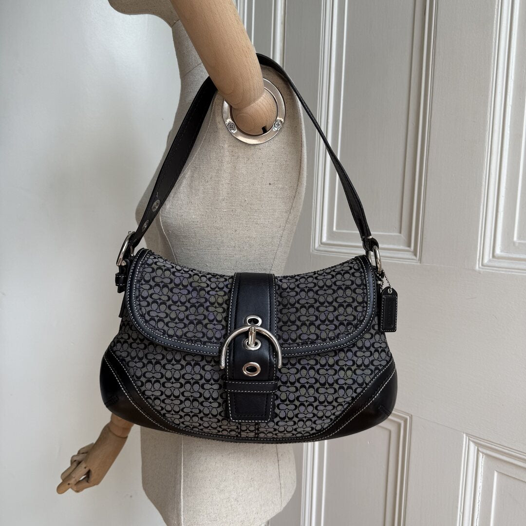 Black patterned handbag on a mannequin against a white wall.